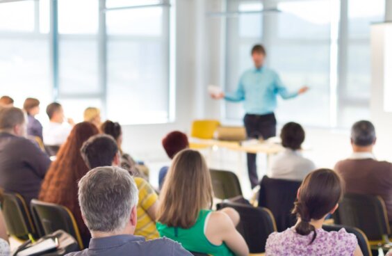 Seated people watch a speaker in a conference room