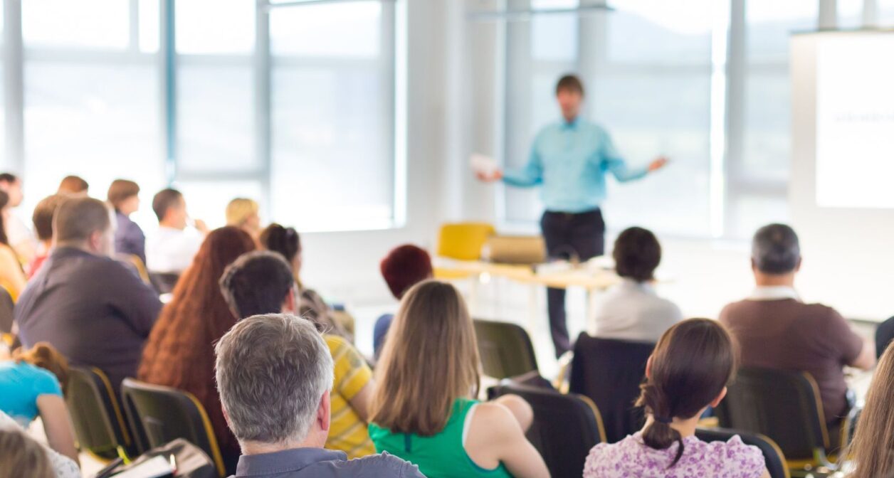 Seated people watch a speaker in a conference room